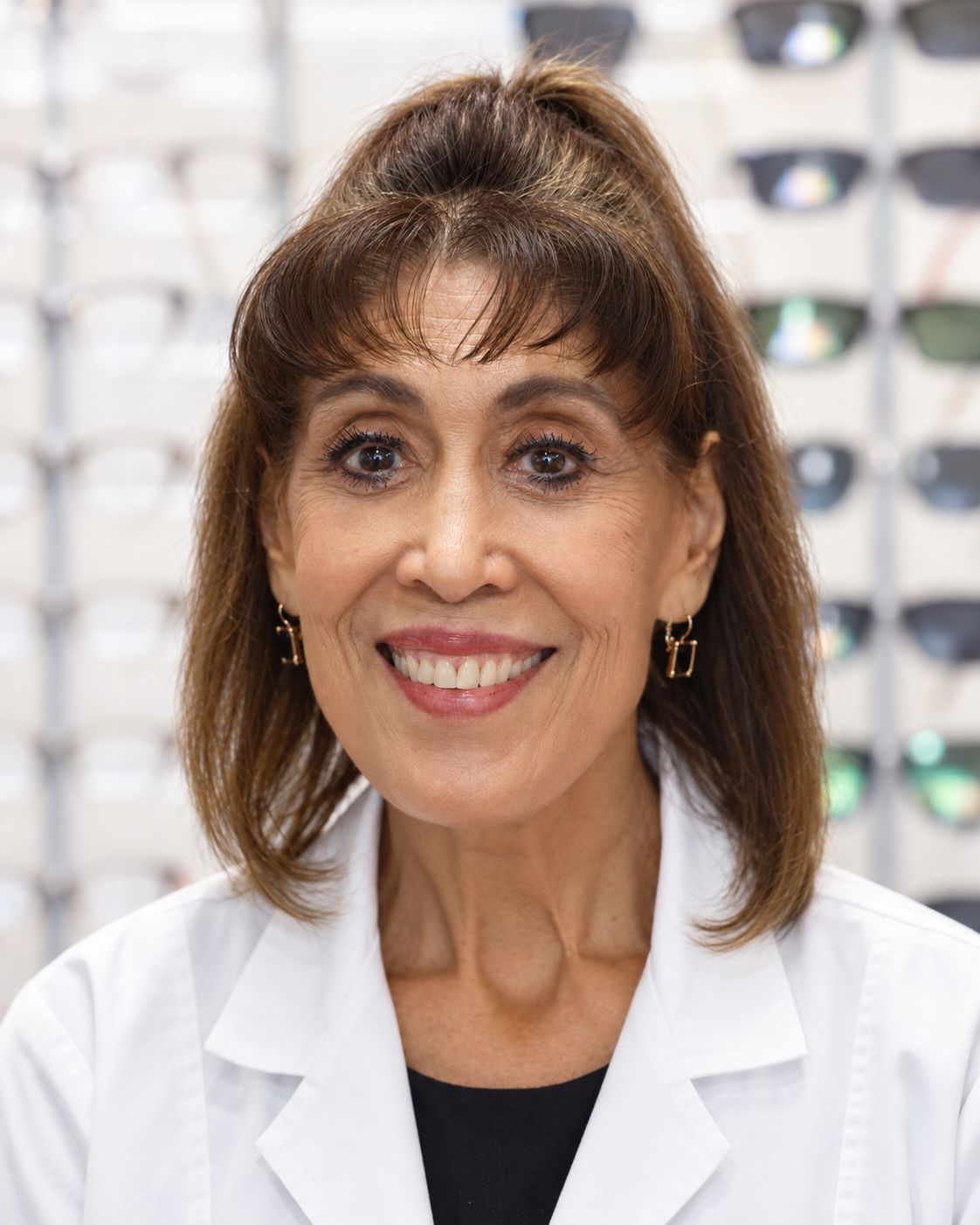 Dr. Rosali Quintanar, OD, in her white coat in front of the frame wall at Affordable Family Vision Center.