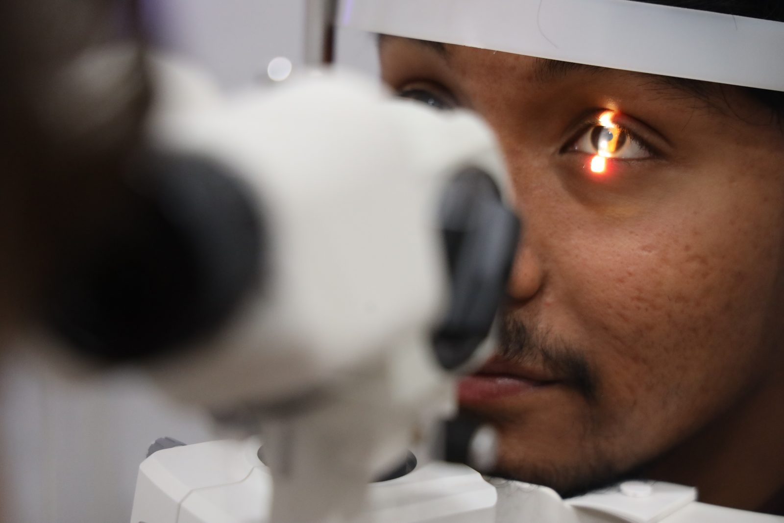 A patient resting their chin on a slit lamp as its light shines into their eye during an eye exam.