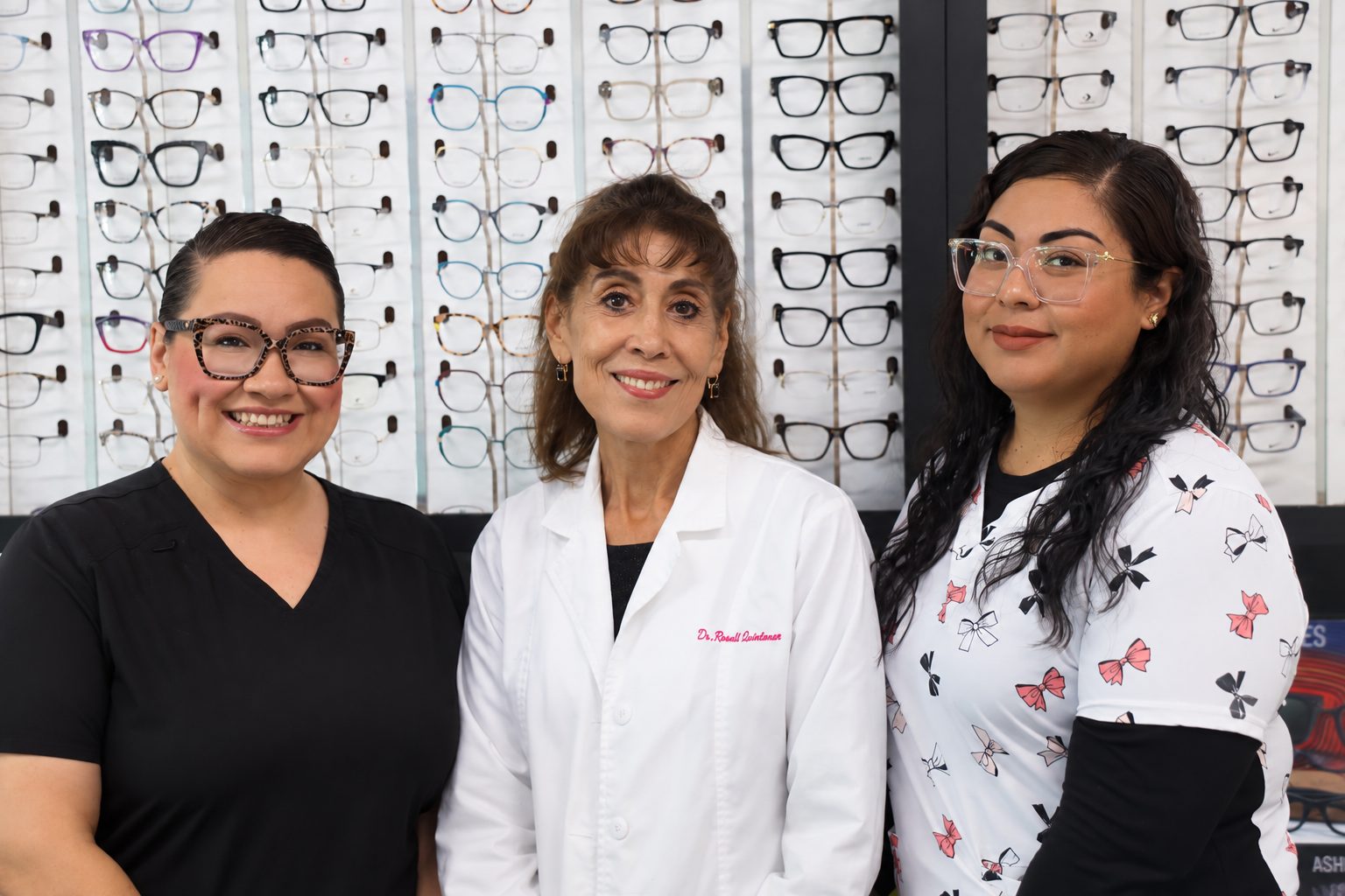 Dr. Rosali Quintanar in her white coat with two members of her team in front of the frame wall.